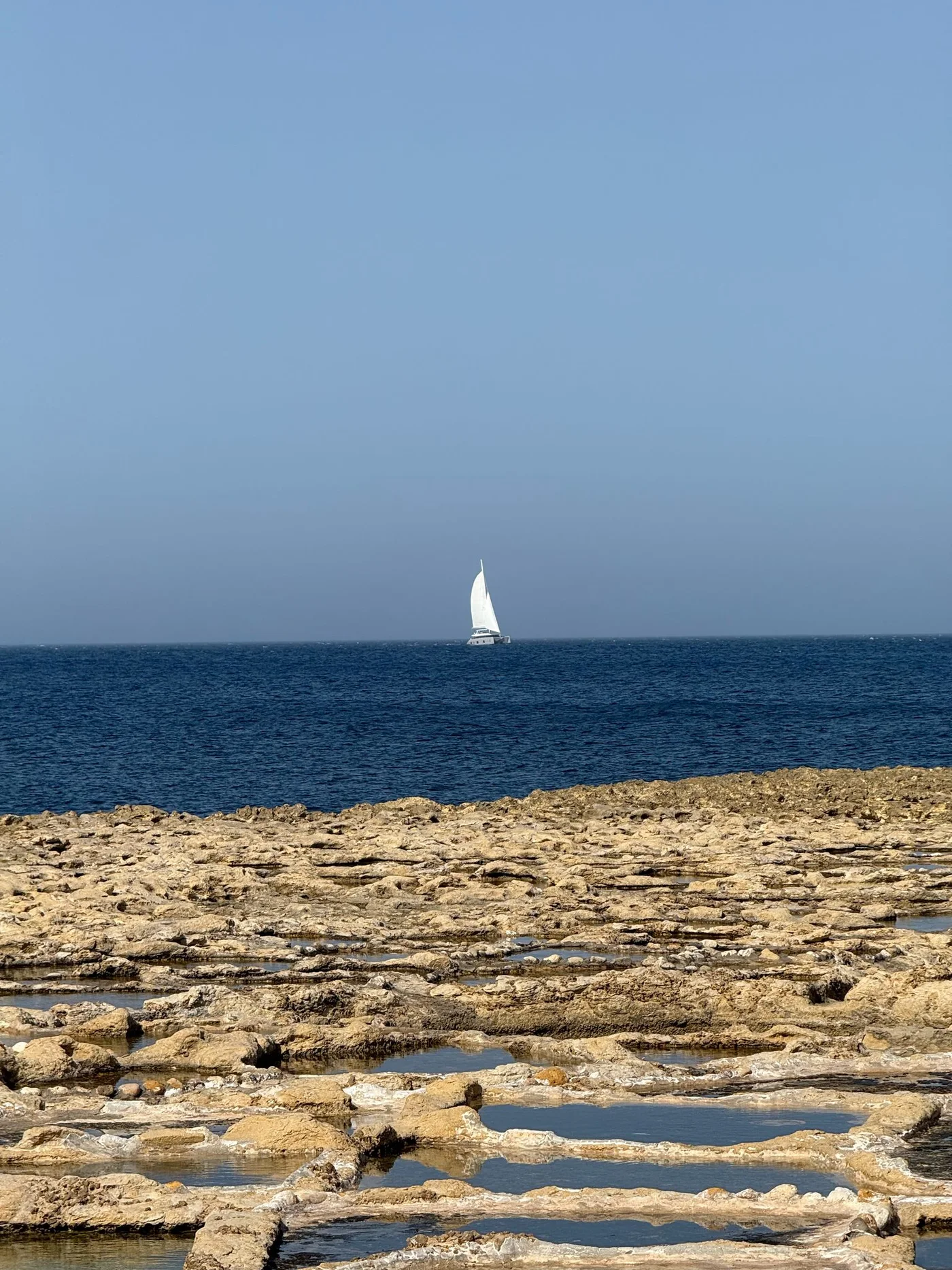 Żaglówka widziana ze skalistego wybrzeża Gozo